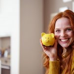 lachende frau hält sparschwein in der hand