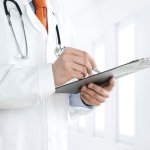 Doctor at the hospital writing notes on the clipboard