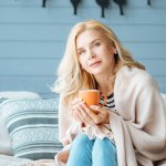 Beautiful woman drinking coffee in cozy bedroom