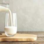 Kefir, milk or Turkish Ayran drink are poured into a glass cup from a bottle. A glass stands on a wooden stand on a rustic wooden table. Place for text